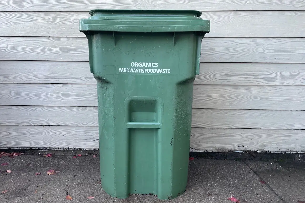 A green compostables cart on a California residential street, filled with yard waste.