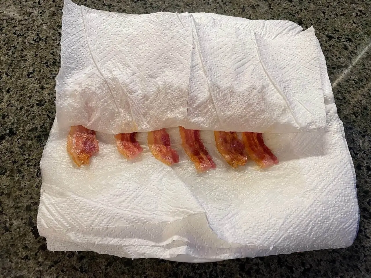 Crisp strips of bacon resting on paper towels after being cooked in a microwave.